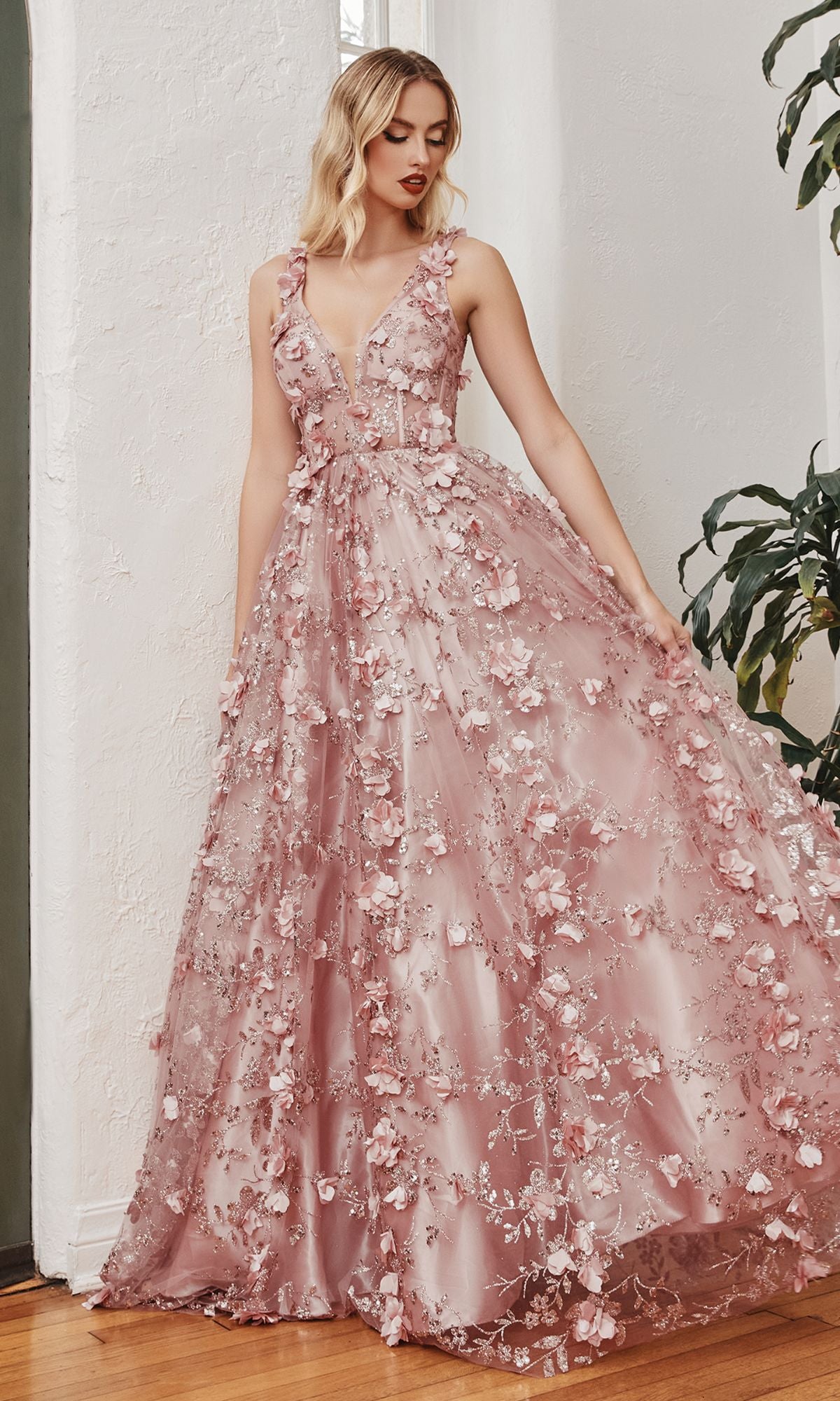 Woman wearing the Long Glitter-Floral A-Line Prom Ball Gown J838, a floor-length sleeveless evening dress with 3D floral embellishments, standing indoors near a potted plant.